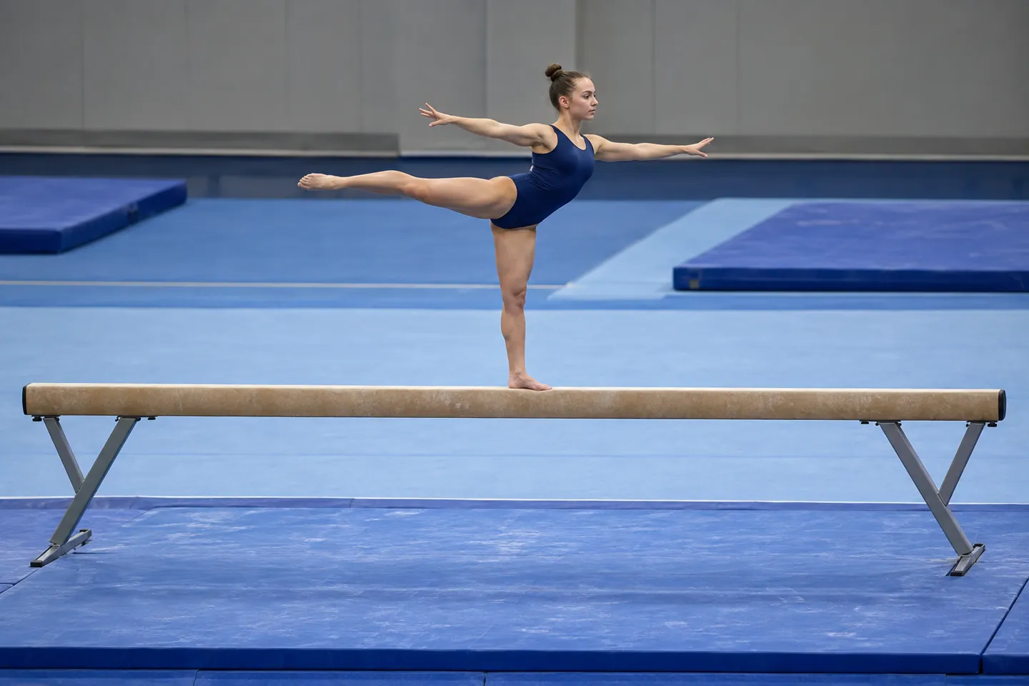 A gymnast balances on a competition balance beam in a gymnasium — the elite apparatus with a 4-inch (10 cm) wide walking surface, the standard answer to how wide is a balance beam.