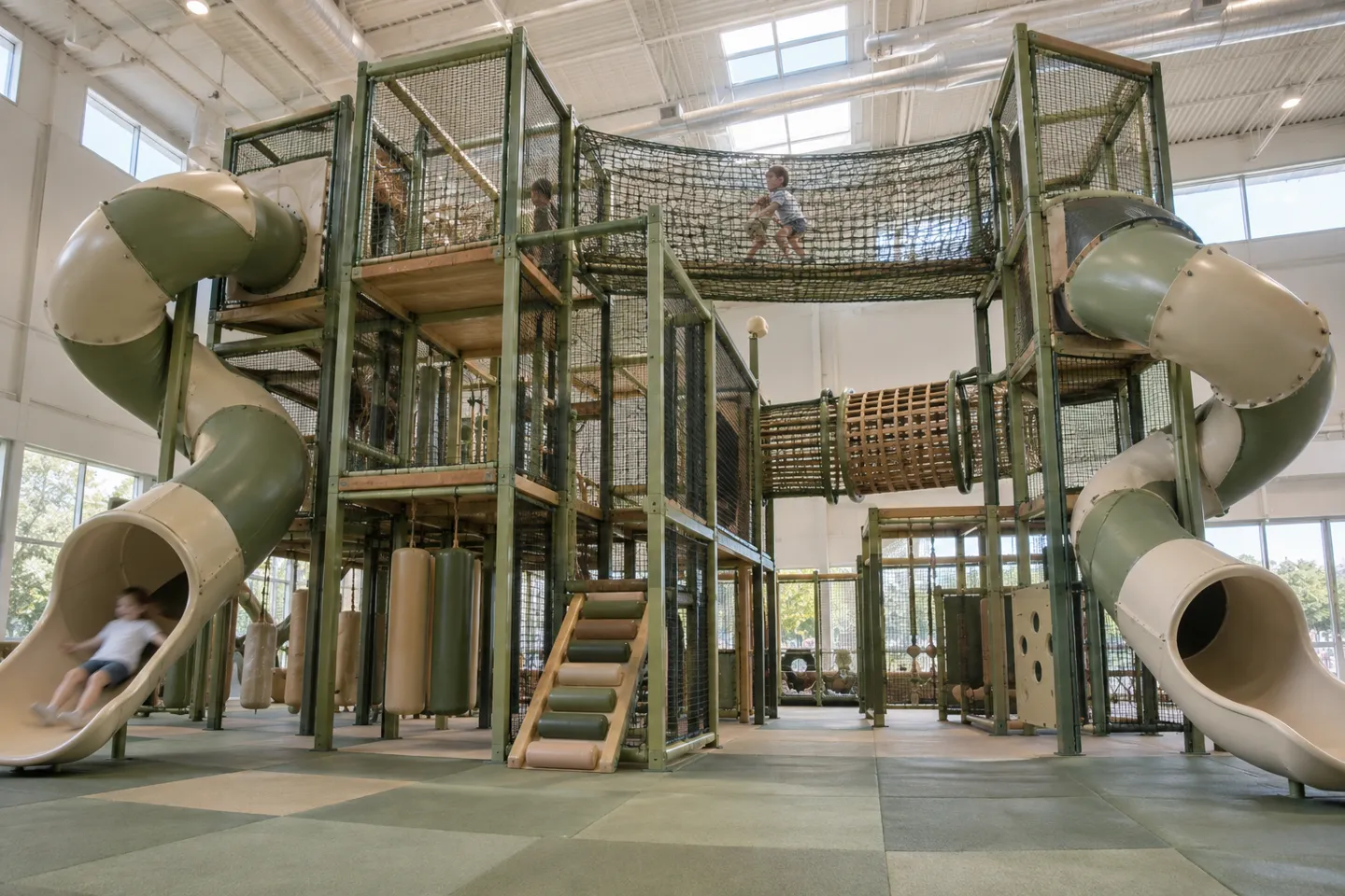 A multi-level steel-frame indoor playground structure with elevated platforms, enclosed tube slides and climbing nets — structure height and play-event count are what drive indoor playground equipment cost at this tier.