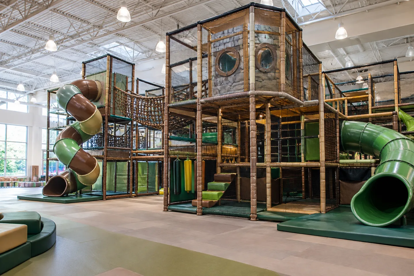 A two-tier multi-level indoor play structure with tube slides and rope bridges, the format quoted per square foot in indoor playground franchise cost budgets