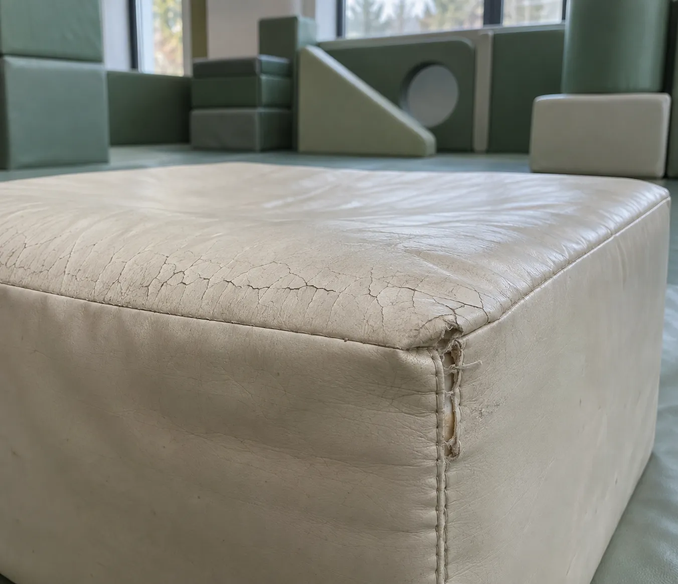 A worn soft play block in a play centre with a cracked vinyl cover and a loosened corner seam, typical end-of-life soft play material failure.